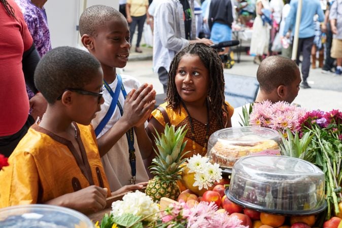 Sulayman Nabilla, 11, stands with Anike Quiones, 9, and prepares to cast offerings into the Schuylkill River as offerings to Osun, the Yoruba Goddess of the River during the Odunde Festival in Philadelphia on Sunday, June 10, 2018. (Natalie Piserchio for WHYY News) 