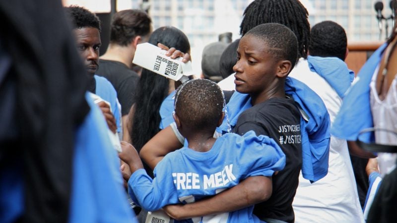 Shaatwion Moore, 21, pours water over her son,  Waalid Mickens, 2, to keep him cool during a rally in support of Meek Mill outside the courthouse where a hearing was taking place. (Emma Lee/WHYY)