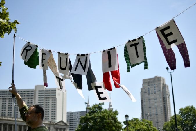 Dan Rothenberg of South Philadelphia holds up a sign made of hand-me-downs he once wore and which his daughter recently grew out of as he, joined by his family participates in a rally to protest Trump's immigration policies on Saturday in Philadelphia. (Bastiaan Slabbers for WHYY)