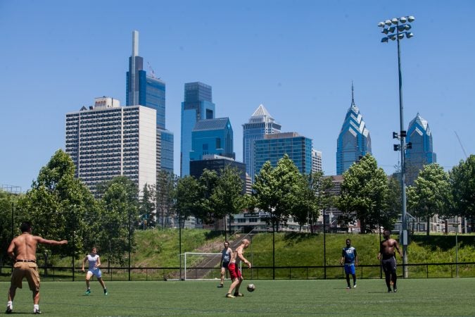 People play soccer on a field with the Philadelphia skyline in the background.