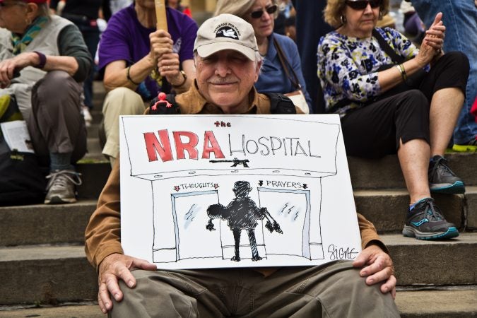 Ronald Instep holds up a Signe Wilkinson cartoon at the rally. (Kimberly Paynter/WHYY)