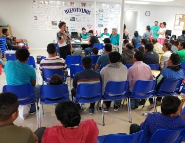 About 100 newly arrived immigrants listen to a volunteer walk them through the process to seek asylum at a Catholic Charities respite center in McAllen, Texas. (Mose Buchele/KUT)