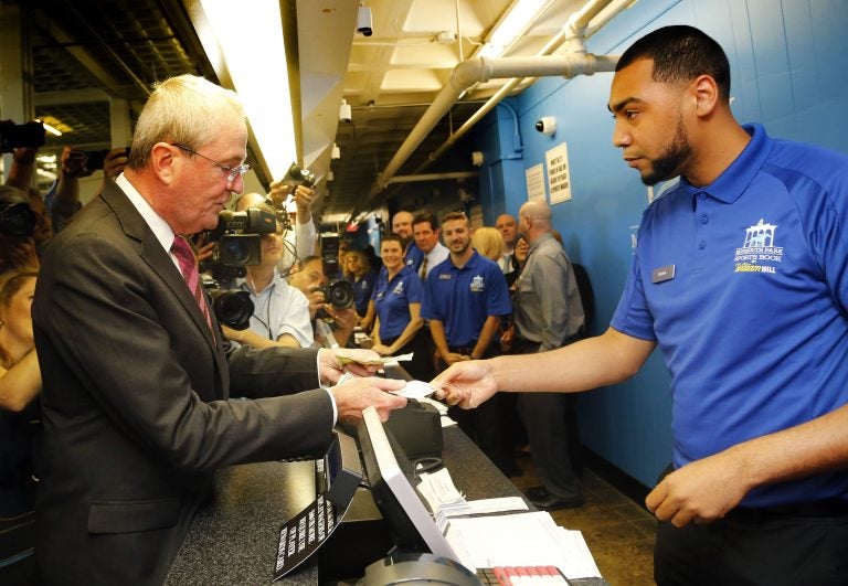 New Jersey Gov. Phil Murphy makes the first wager with Monmouth Park Sports Book ticket writer Quentin Harris, at Monmouth Park Racetrack Thursday in Oceanport, New Jersey. Major League Baseball has circulated a memo to teams, forbidding them and their broadcasting affiliates from accepting advertisements from sports betting outfits, such as Monmouth. (AP Photo/Noah K. Murray)