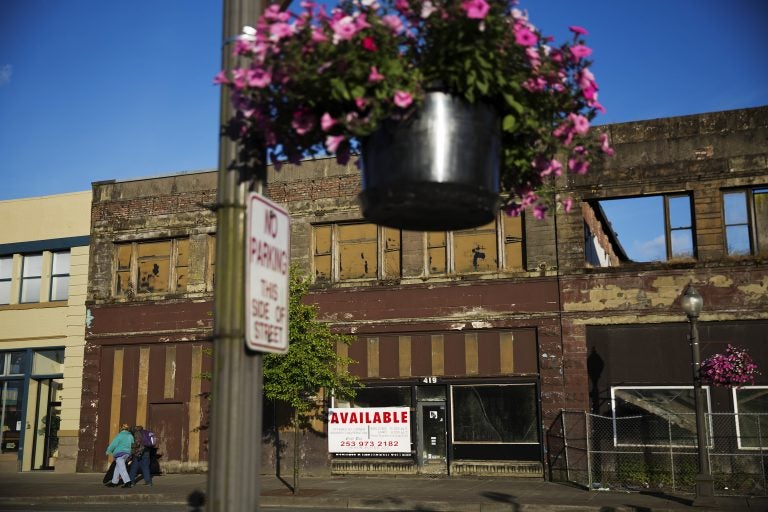 In this June 16, 2017, file photo, dilapidated storefronts stand along baskets of pink petunias that hang from light posts all over town, watered regularly by residents trying to make their city feel alive again in Aberdeen, Wash. From drivers paying more for gas and families bearing heavier child care costs to workers still awaiting decent pay raises to couples struggling to afford a home, people throughout the economy are straining to succeed despite the economy’s gains. (AP Photo/David Goldman, File)