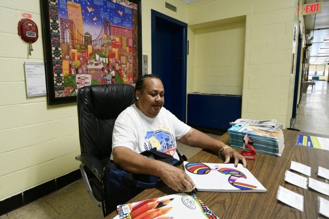 Ms. Robin Griffin shows her own work as she sits at the front desk, surrounded by replicas of works of art from the collection of the Philadelphia Museum of Art, ahead of an announcement of the Inside Out art education program at Edward Gideon Elementary School, on Tuesday June 12, 2018. (Bastiaan Slabbers for WHYY)