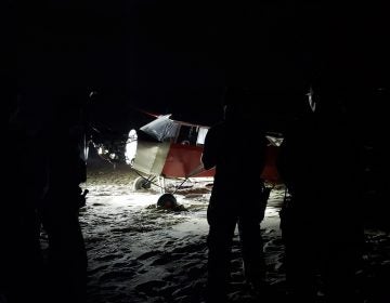 In this June 24, 2018 photo, Coast Guard personnel stand in front of a plane on a secured beach on the southeast side of the U.S. Coast Guard Training Center Cape May after it landed illegally and there was no sign of the pilot. The Coast Guard says officers became aware of the incident when the plane was spotted on closed-circuit cameras. (Petty Officer 2nd Class Richard/U.S. Coast Guard via AP)
