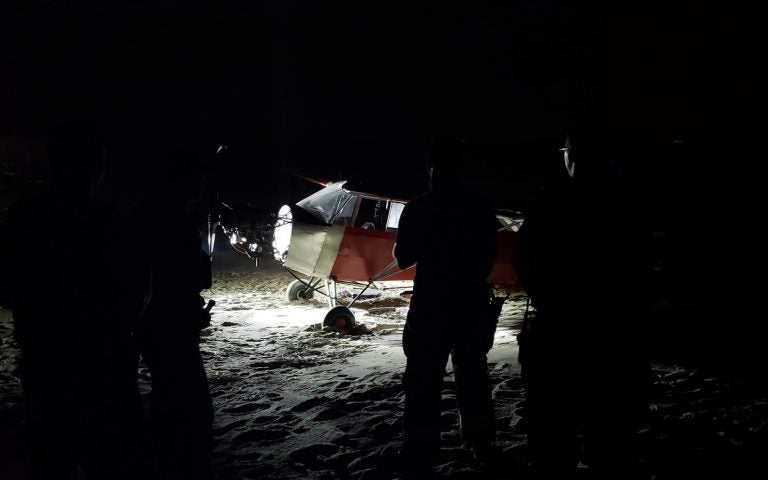 In this June 24, 2018 photo, Coast Guard personnel stand in front of a plane on a secured beach on the southeast side of the U.S. Coast Guard Training Center Cape May after it landed illegally and there was no sign of the pilot. The Coast Guard says officers became aware of the incident when the plane was spotted on closed-circuit cameras. (Petty Officer 2nd Class Richard/U.S. Coast Guard via AP)