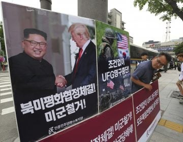 A photo of President Trump and North Korean leader Kim Jong Un is on display as a member of People's Democratic Party stands in opposition of military exercises between the United States and South Korea near the U.S. embassy in Seoul on Tuesday. (Ahn Young-joon/AP)