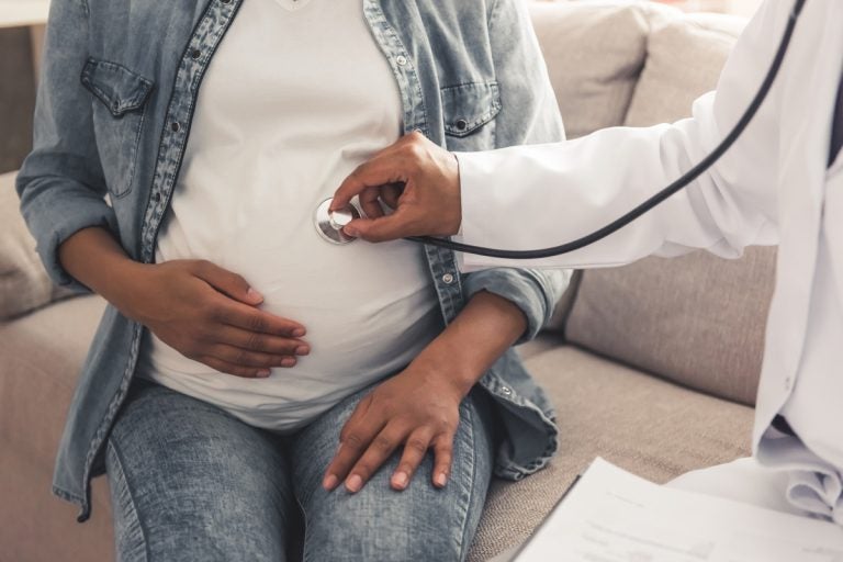 A doctor holds a stethoscope on a pregnant person's belly.