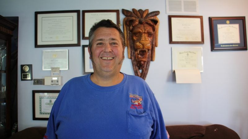 Greg Crance, the founder of The Famous River Hot Dog Man stands in his home office in Southampton. All four of his sons help to run the family business and have either completed their master's degrees or are working toward them. Their diplomas decorate the walls of his office. (Emma Lee/WHYY)