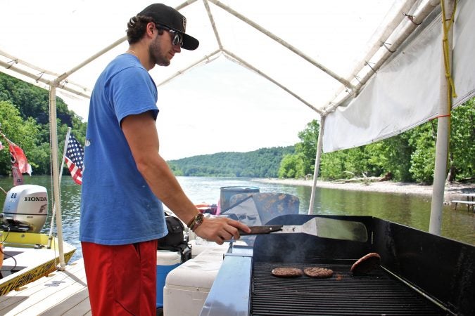 College student Ryan Matthews flips burgers at the Famous River Hot Dog Man, a summer job he has held for four years. (Emma Lee/WHYY)