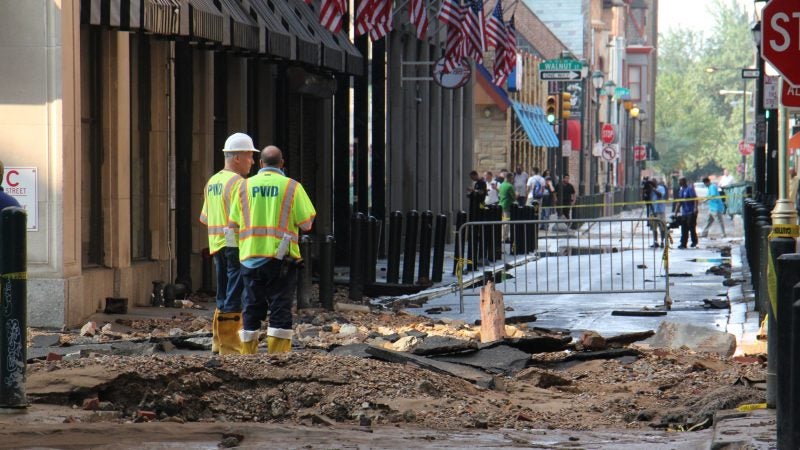 Water department employees stand at the site of the water main break at Sansom and Juniper streets. (Emma Lee/WHYY)