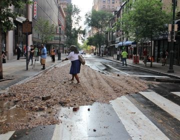 A pedestrian at Walnut and Juniper streets steps over a pile of debris left behind by a massive water main break in Center City. (Emma Lee/WHYY)