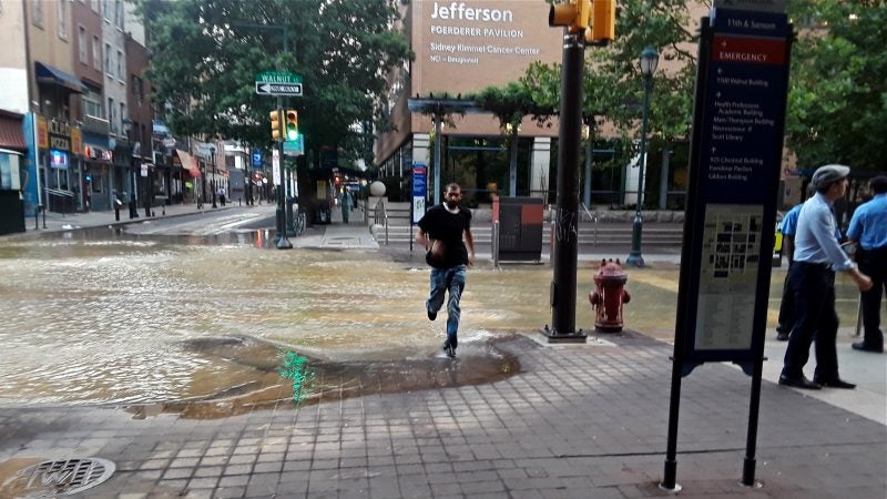 A pedestrian sprints through the flooded intersection at 11th and Walnut streets after a water main break in Center City. (Trenae Nuri/WHYY)