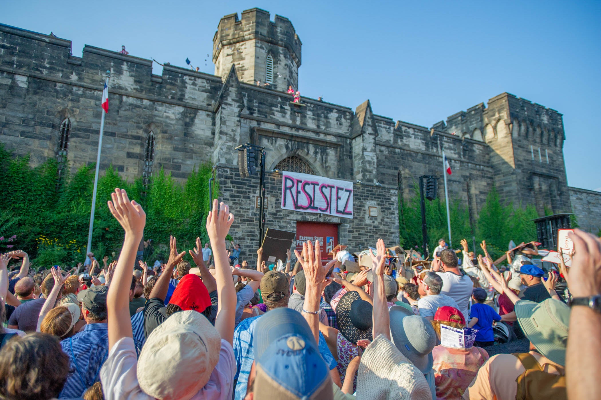 People in the crowd reach for the sky as Marie Antoinette and her minions throw Tastykakes from the top of the Eastern State Penitentiary wall. 