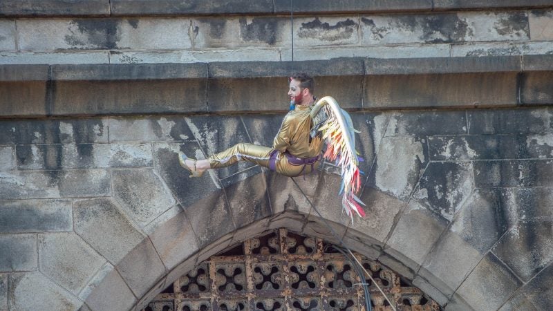 Reprising his role as Edith Piaf for the last time, John Jarboe rappels from the tower of Eastern State Penitentiary wearing a gold lame jump suit, wings, and gold heels. (Jonathan Wilson for WHYY)