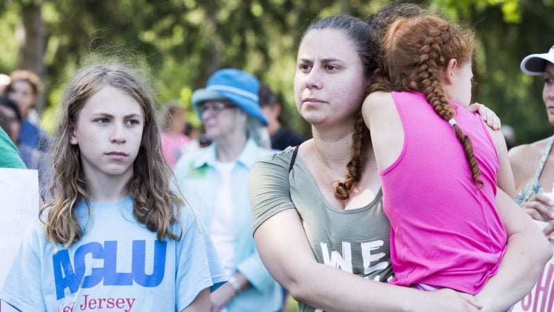 Ruth Barreiro (center) and her children (from left), Joshua and Alexandria, are stone faced as they listen to a speaker denounce the Berks County Residential Center at a vigil held on July 15. Barreiro and her children traveled from Vineland, New Jersey, to attend the rally. (Rachel Wisniewski for WHYY)