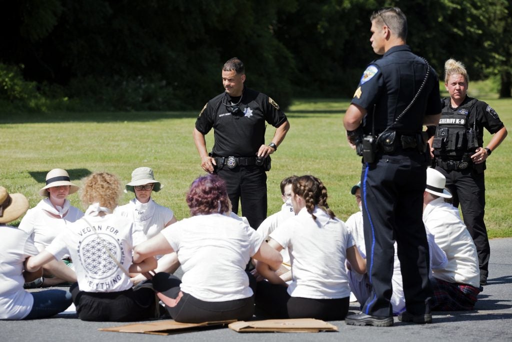 Berks County police officers stand by as a group of eighteen protesters link arms while seated in the road outside of the Berks County Residential Center on July 15. Despite being told that they would risk arrest, the demonstrators decided to sit anyway.