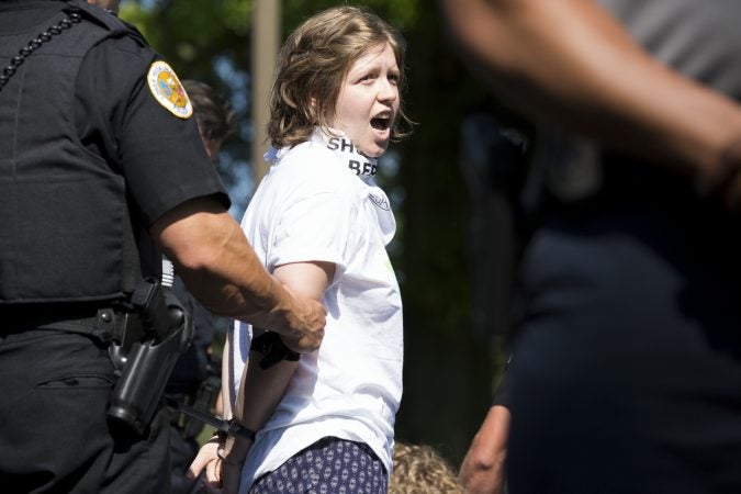 A demonstrator is arrested at the Vigil to Shut Down Berks on the afternoon of July 15. Seventeen arrests were made after group blocked a road outside the detention facility in Leesport, Pa., which is used to house immigrant families who are seeking asylum or fighting deportation. (Rachel Wisniewski for WHYY)