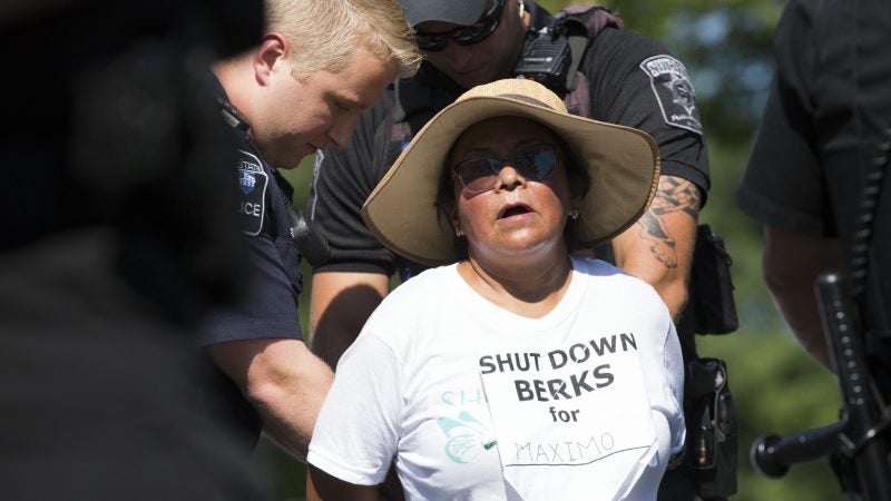 A demonstrator is arrested at the Vigil to Shut Down Berks on the afternoon of July 15. Seventeen arrests were made after group blocked a road outside the facility, which is used to house immigrant families. (Rachel Wisniewski for WHYY)