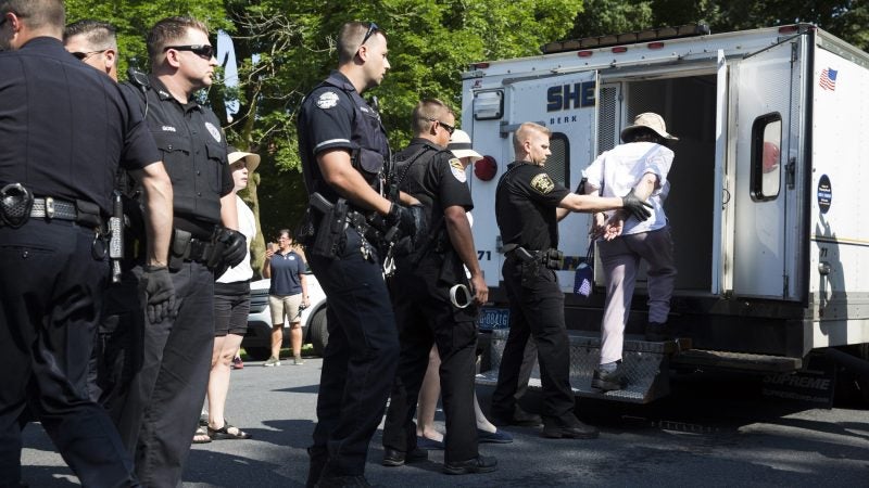 A demonstrator is led into a police van after being arrested at the Vigil to Shut Down Berks on July 15. Seventeen arrests were made after protesters blocked a road outside the detention facility, which houses immigrant families who are fighting deportation. (Rachel Wisniewski for WHYY)