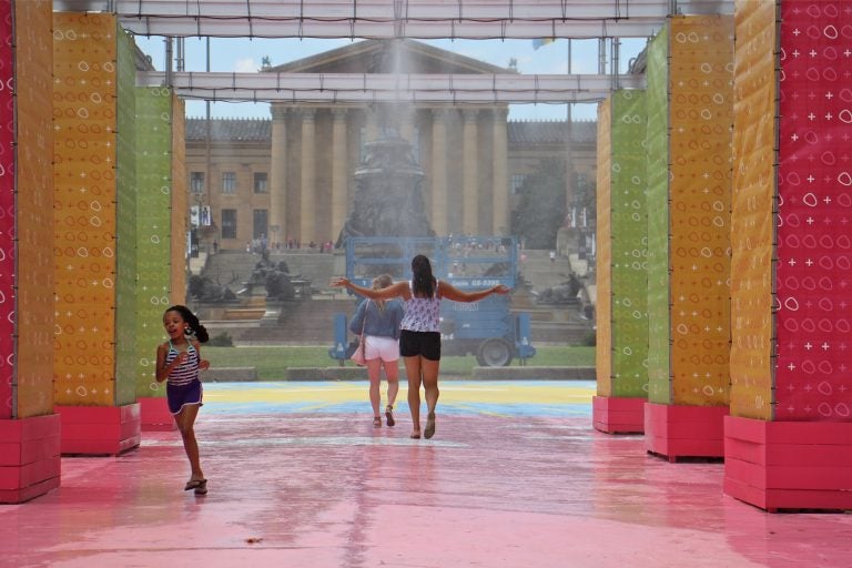 People cool off in the mister at the Eakins Oval pop-up park. (Emma Lee/WHYY)
