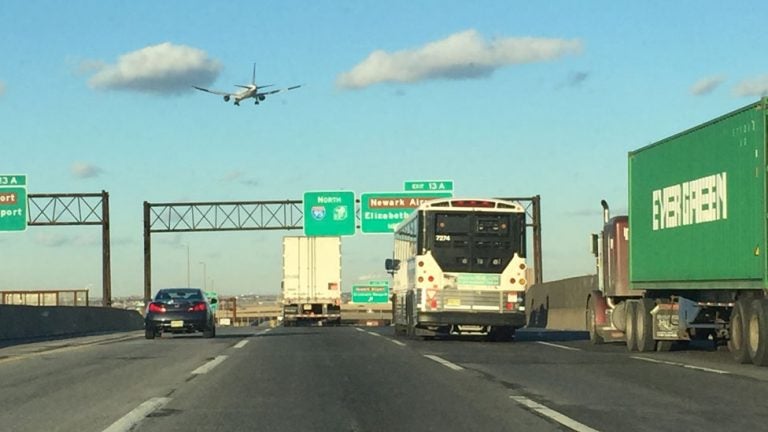 Cars and trucks are visible driving northbound on the New Jersey turnpike on a sunny day.