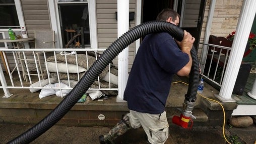 A volunteer hauls a hose past flooded homes as he and others help pump water out Wednesday, July 25, 2018, in Tremont, Pa. Days of drenching rains are closing roads, sending creeks and streams over their banks and prompting some evacuations in central Pennsylvania. (Jacqueline Larma/AP Photo)