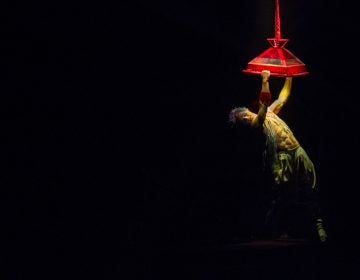 Joey Arrigo, as the character Waz, performs on a lighting fixture in 