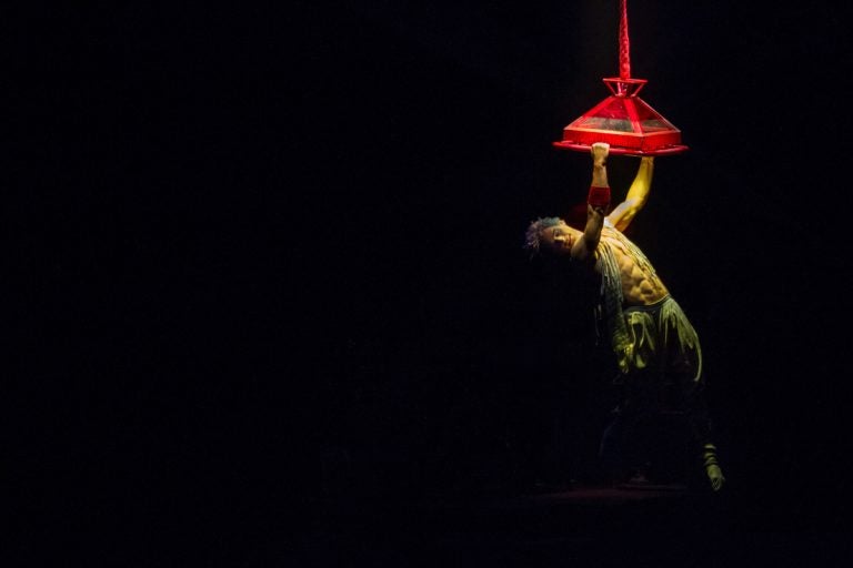 Joey Arrigo, as the character Waz, performs on a lighting fixture in 