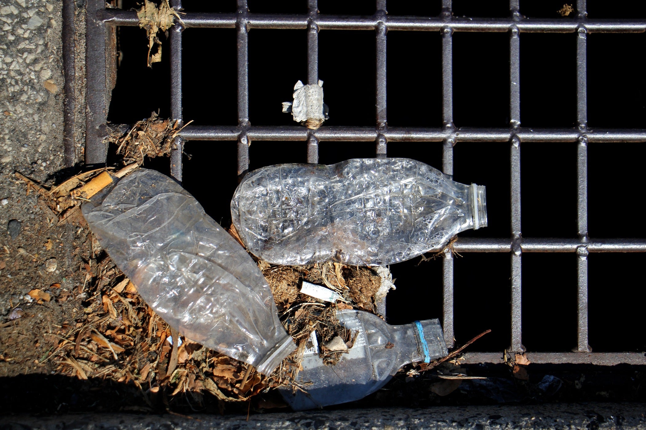 Plastic bottles accumulate on the grate of a storm drain. 