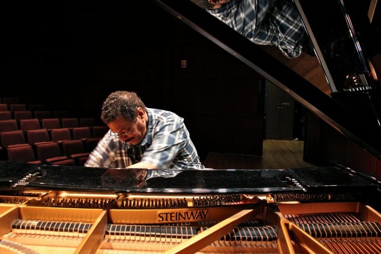 Composer and educator Alfonso Fuentes plays a black Steinway grand piano under a spotlight in a dark and empty auditorium at Princeton University