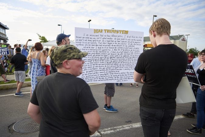 Trump supporters are seen reading an open letter from Trump Protesters at a demonstration outside of the Make America Great Again rally in Wilkes-Barre, Pa., on August 2, 2018. (Natalie Piserchio for WHYY)