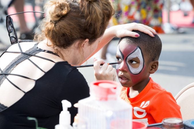 Chrissy Jones (left) paints the face of Kadeem Gaines, 3, as Spiderman at a booth advertising The Met Philadelphia at Broad and Poplar Streets on August 11, 2018. (Rachel Wisniewski for WHYY)