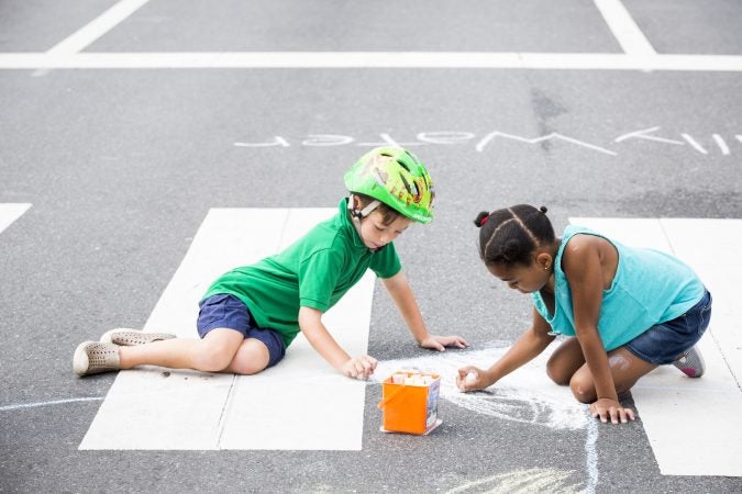 Geffen Reinherz, 5 (left), and Skyla Car, 7, draw with chalk at Broad and Poplar Streets while Broad Street is closed off for Philly Free Streets on August 11, 2018. (Rachel Wisniewski for WHYY)
