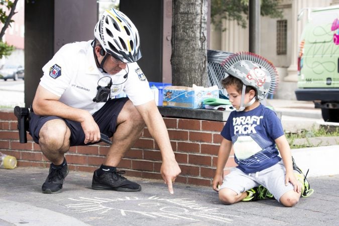 Philadelphia Police Captain Javier Rodriguez compliments Logan Miller, 5, on a monster he has drawn with chalk at Broad Street and Ridge Avenue on August 11, 2018. (Rachel Wisniewski for WHYY)