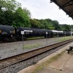 A black freight train, operated by Norfolk Souther, speeds by on a track, as seen from the former train station in Phoenixville, PA.