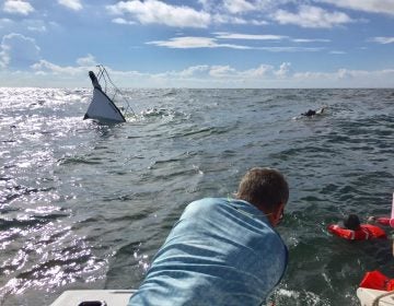 The Miss Addison II crew performing a rescue as a boat sinks in the background.  