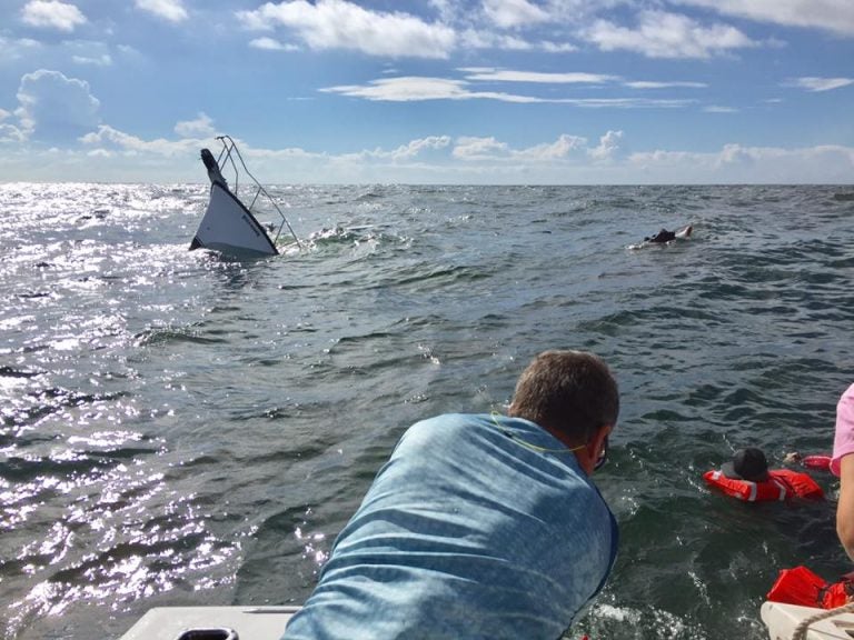 The Miss Addison II crew performing a rescue as a boat sinks in the background.  