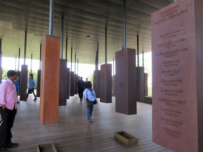 This April 28, 2018 photo shows visitors looking at markers bearing the names of lynching victims at the National Memorial for Peace and Justice in Montgomery, Ala. The memorial includes some 800 markers, one for each county in the U.S. where lynchings took place, documenting the killings of more than 4,400 individuals between 1877 and 1950. (AP Photo/Beth J. Harpaz)