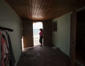 Rosa Elena Mastache Dominguez looks out at the beach through a door that once led to the back of her family home. Hurricane Maria shrunk the beach behind her home, then another storm brought waves that destroyed the structure. (Irina Zhorov/WHYY)