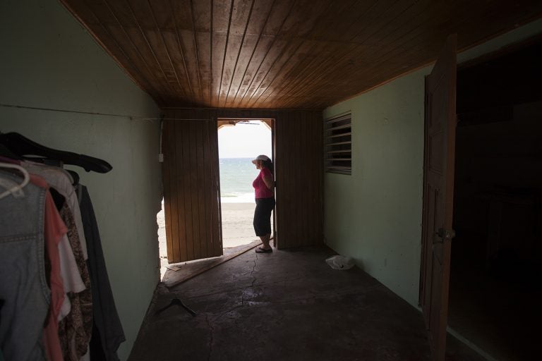 Rosa Elena Mastache Dominguez looks out at the beach through a door that once led to the back of her family home. Hurricane Maria shrunk the beach behind her home, then another storm brought waves that destroyed the structure. (Irina Zhorov/WHYY)