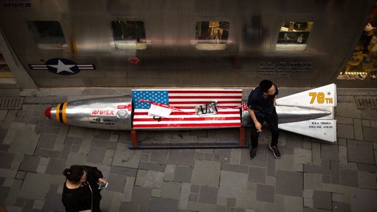 A man sits on a promotional gimmick in the form of a bomb and the U.S. flag outside a U.S. apparel shop at a shopping mall in Beijing. China says it’s girded for a trade war with the U.S. and can give as good as it gets, but behind the official bravado lies a deep unease over trade friction with Washington. (AP Photo/Mark Schiefelbein)