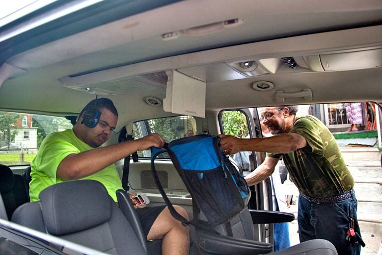 Linwood Bellamy (right) hands his son, Kareem Bellamy, 20, his lunch bag as he loads into the taxi that will take him to school. An increasing number of Philadelphia students are relying on cabs to transport them to and from school. (Emily Cohen for WHYY)