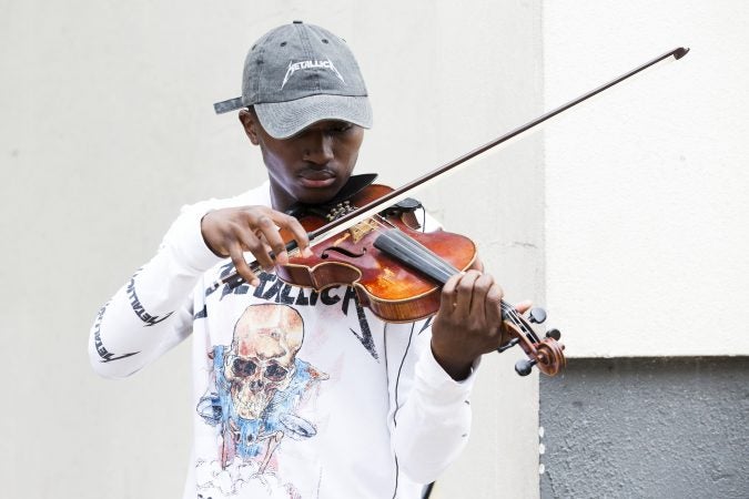 Rickey Turner, 21, plays the violin for passers-by outside of the Made in America festival. (Rachel Wisniewski for WHYY)