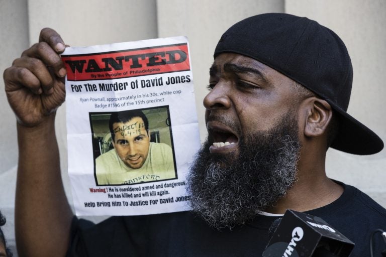 Isaac Gardner speaks while holding up a photo of David Jones