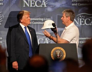 President Donald Trump accepts a hard hat from National Electrical Contractors Association President David Long. Trump closed the NECA convention in Philadelphia with a speech on job creation and training. (Emma Lee/WHYY)