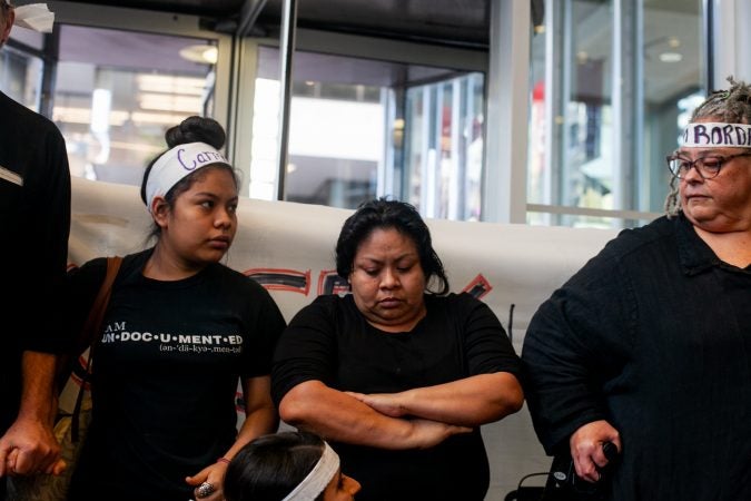 Undocumented immigrant Carmela Apolonio Hernandez and her daughter Keyri Artillero Apolonio (left) block an entrance with local clergy in to the lobby of 2000 Market Street Wednesday after demanding a meeting with U.S.  Sen. Bob Casey at his office. (Brad Larrison for WHYY)
