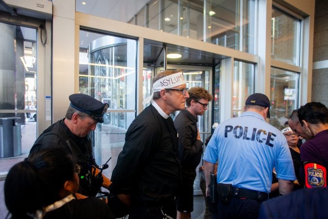 Police handcuff the Rev. Robin Hynicka after he refused to move away from the doors at 2000 Market Street. (Brad Larrison for WHYY)