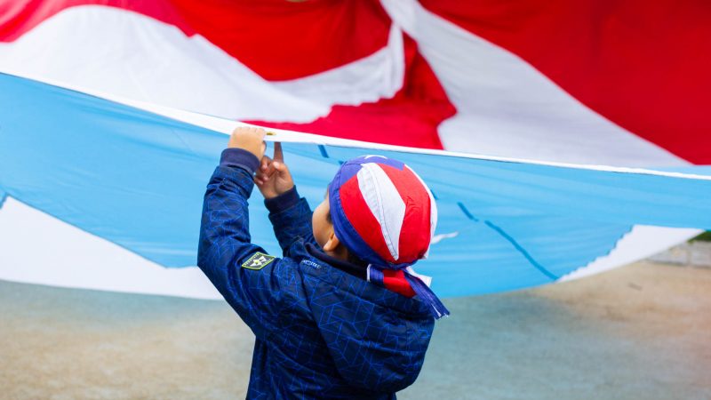 A boy plays with a large Puerto Rican flag that was laid it at the steps of the Philadelphia Museum of Art. A group of activist marched the Benjamin Franklin Parkway with the flag to commemorate the people who died in Hurricane Maria in Puerto Rico. (Miguel Martinez for WHYY)